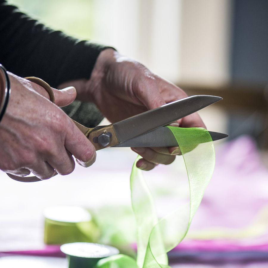 hands using a pair of large scissors cutting green ribbon wrapping a gift