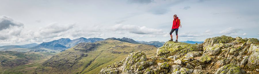 Teenage girl hiker standing on a mountain summit overlooking a panoramic vista of green valleys and rocky peaks high in the picturesque natural landscape of the Lake District National Park, Cumbria, UK. ProPhoto RGB profile for maximum color fidelity and gamut.