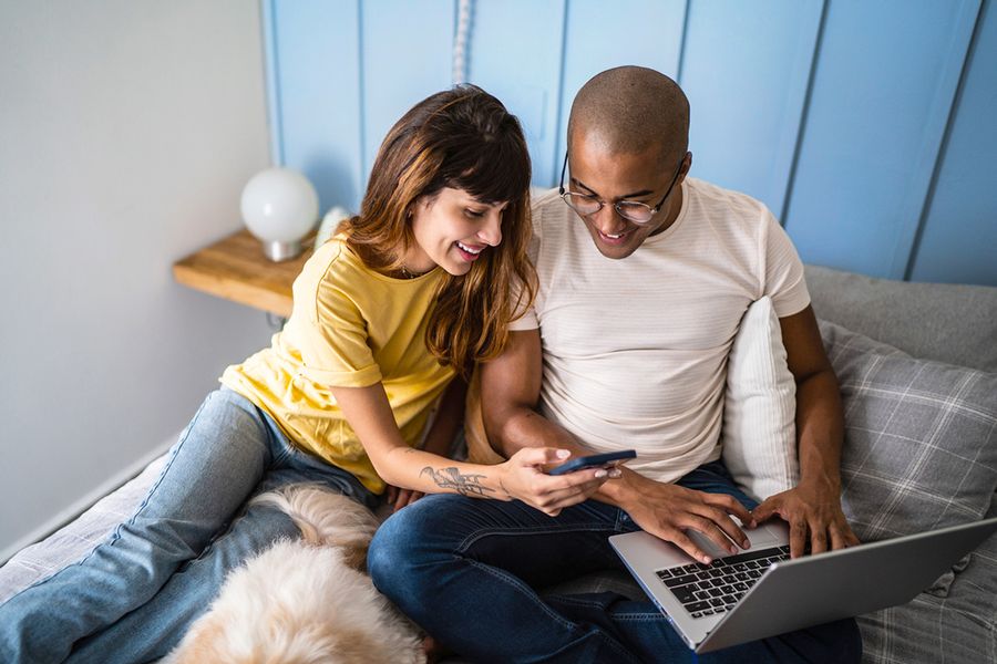 A couple looking at a phone. A man looking at a laptop.