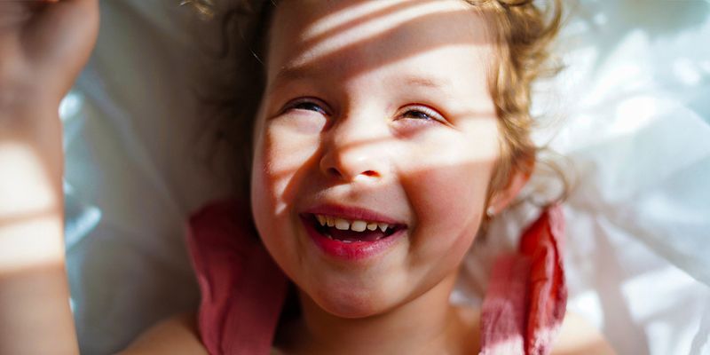 A smiling little girl with sunlight and soft shadows across her face, inspiring Photobox tips on how to take good pictures in bright sunlight.